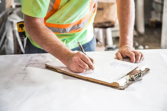 Mains d'un artisan en gilet de chantier remplissant un bloc-notes