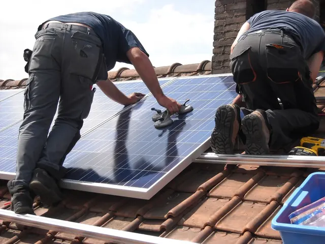 Deux artisans posent des panneaux solaires sur un toit en tuiles